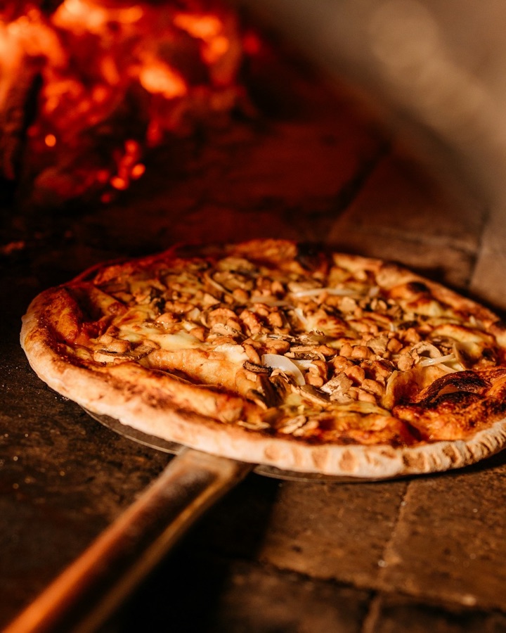 Pizza auf dem Schieber vor dem Holzofen