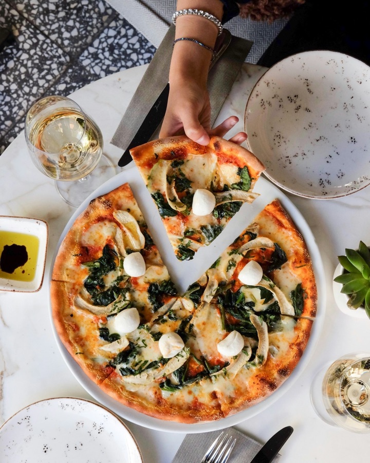 Hand nimmt ein Stück Pizza vom Teller