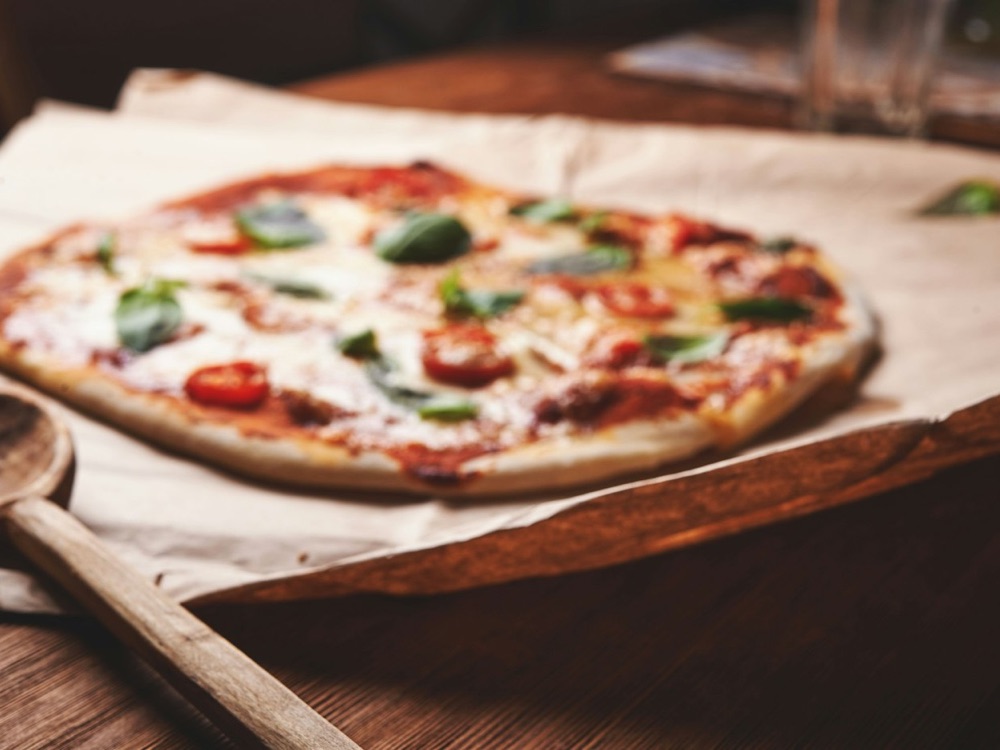 Pizza Margherita auf Backpapier und Holzbrett