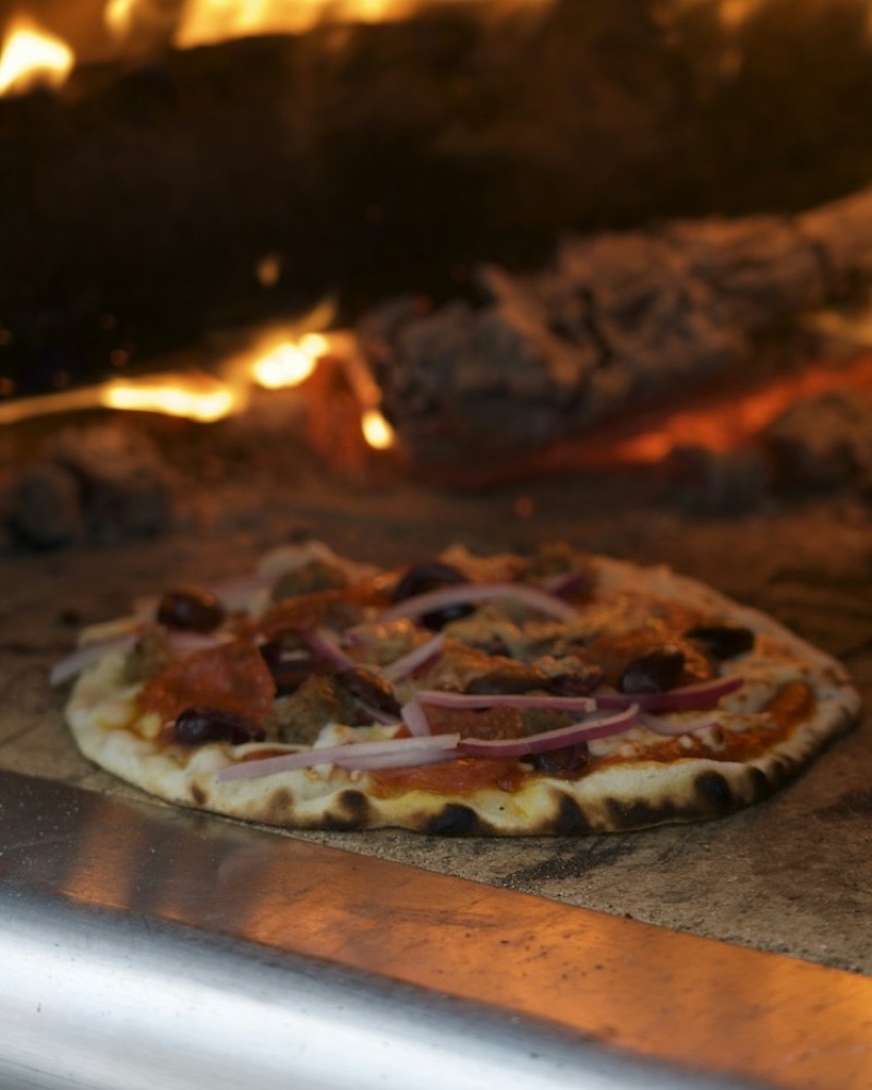 Pizza backt im Holzofen neben dem Feuer