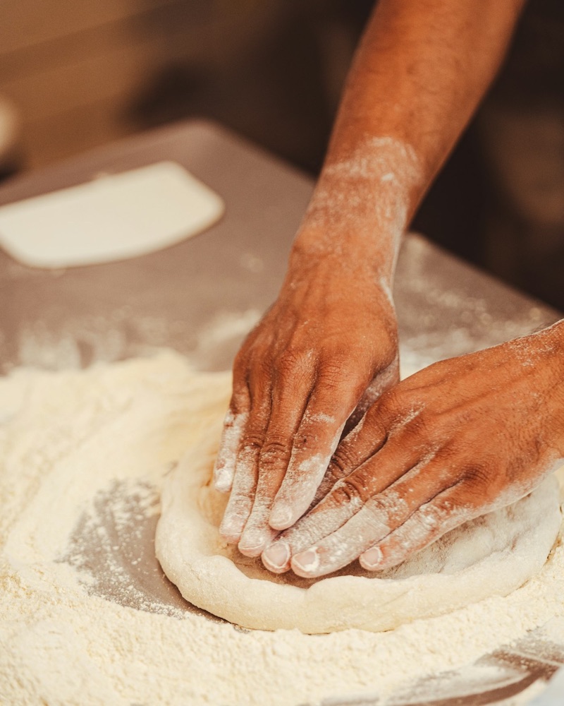 Hände drücken Pizzateig auf bemehlter Arbeitsfläche aus